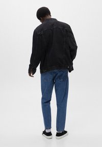 Chaqueta de mezclilla negra de corte holgado, con mangas largas, cierre de botones y canesú trasero, combinada con jeans azules de pierna recta.