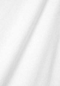 Gros plan d'un tissu blanc doux avec un tissage visible et des plis délicats.