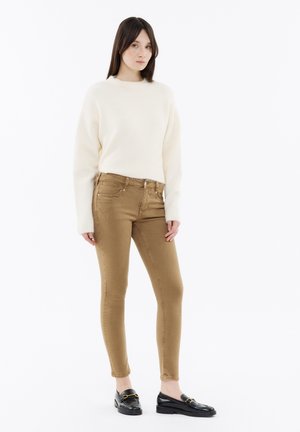 Cream sweater with ribbed hem, tan skinny jeans with five pockets and light whiskering, black loafers with gold accent.