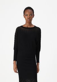 Melna ribota adīta džemperis ar garām piedurknēm un apkakles izgriezumu, ar teksturētu rakstu un pieguļošu jostu, apvienots ar atbilstošām svārkiem.