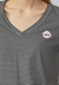 Zwart-wit gestreepte V-hals t-shirt met korte mouwen. Heeft een ronde roze "JOY" logo aan de linkerkant nabij de halslijn.