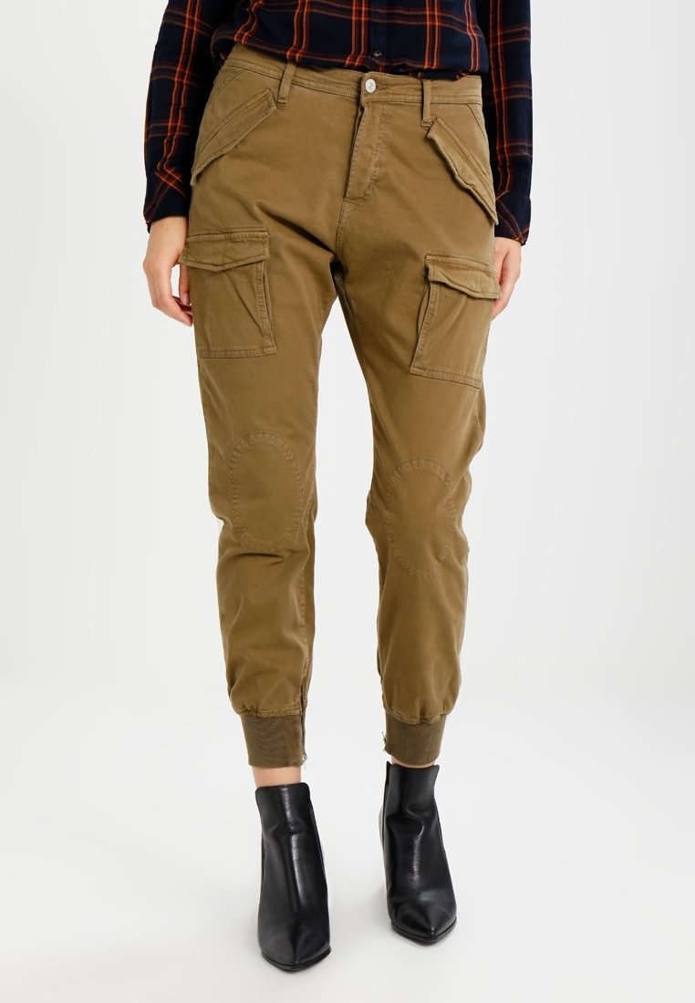 Khaki cargo kalhoty s několika předními kapsami, elastickými manžetami a kolenními záplatami; v kombinaci s černými kotníkovými botami. Bavlněný materiál.