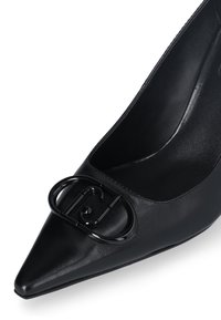 Bottines à talon en cuir noir à bout pointu, présentant un accent en logo noir brillant sur le devant et une doublure intérieure lisse.