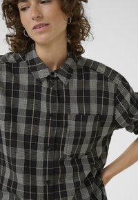 Schwarz-weißer karierter Button-Up-Hemd mit Kragen, Brusttasche und strukturiertem Stoff; hat unterschiedliche Karomuster und schwarze Knöpfe.