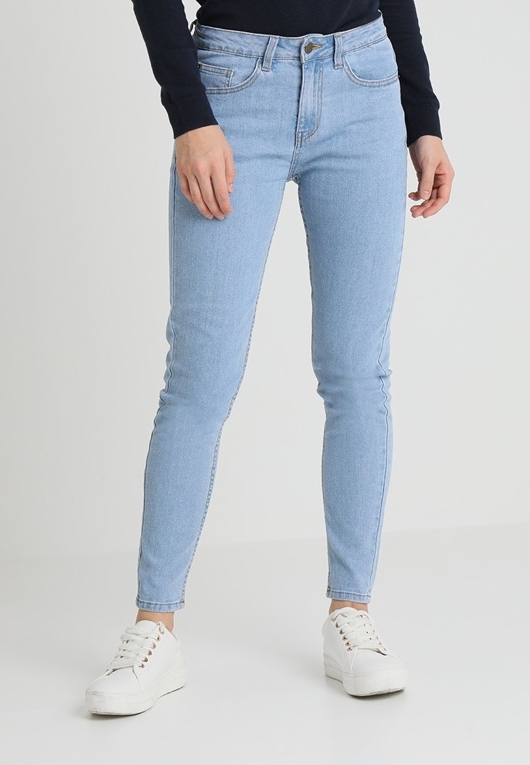 Jean skinny bleu clair en denim, avec cinq poches, une fermeture éclair et une silhouette ajustée. Associé à des baskets blanches.