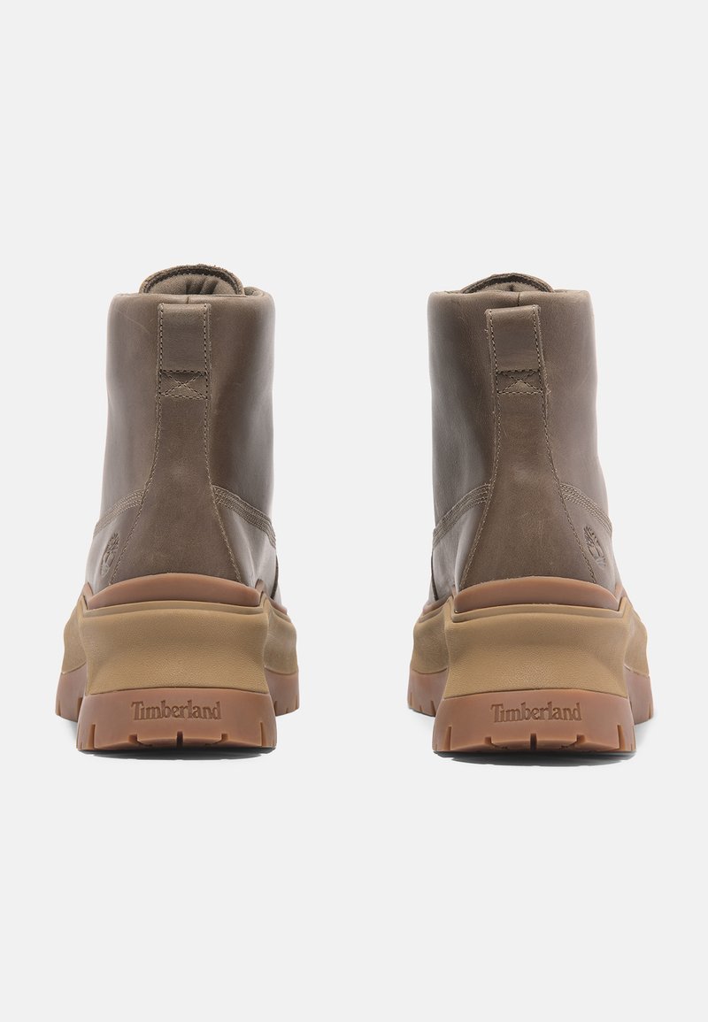 Stivali alla caviglia in pelle marrone con suola in gomma, caratterizzati da accenti beige in contrasto, punta arrotondata e dettagli di cucitura minimi sul retro.