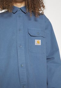 Lichtblauw overhemd met knopen in een zachte, gelijkmatige stof. Beschikt over een borstzak met een rechthoekig logo-opdruk en een klassiek kraagdesign.