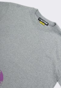 T-shirt in cotone grigio con collo rotondo classico, con una grande grafica viola sul davanti e un'etichetta con la scritta "IUTER" all'interno del collo.