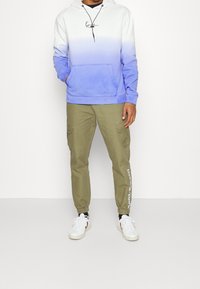 Hooded sweatshirt with a white to blue ombre design, kangaroo pocket, paired with olive green cargo pants featuring side pockets and logo accents.