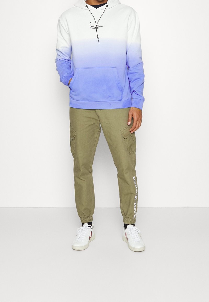 Hooded sweatshirt with a white to blue ombre design, kangaroo pocket, paired with olive green cargo pants featuring side pockets and logo accents.