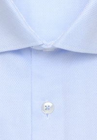 Camicia azzurro chiaro con trama, colletto classico e un singolo bottone argentato sulla patta. Il materiale sembra traspirante e tessuto.