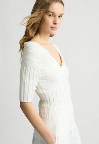 Top bianco a coste con scollo a V profondo e maniche corte, caratterizzato da un dettaglio attorcigliato sul davanti e una silhouette aderente.