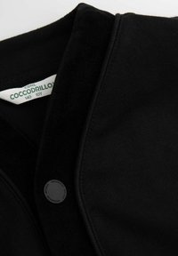 Czarna bawełniana kurtka z teksturowanym kołnierzem, zapięciem na guziki i widoczną metką marki. Materiał jest gładki z lekko miękkim wykończeniem.