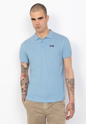 Hellblaues Poloshirt mit kurzen Ärmeln, zwei Druckknöpfen und kontrastierendem gesticktem Logo. Strukturiertes Baumwollgewebe.