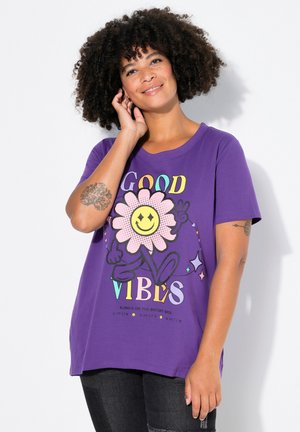 T-shirt en coton violet avec un grand graphique d'une fleur souriante et le texte "BONS FLUX". Manches courtes et coupe décontractée.