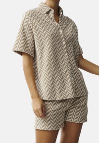 Short-sleeve, button-up pajama set in beige with a herringbone pattern. Made of soft fabric with a relaxed fit and matching shorts.