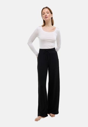 Pantalon noir à jambes larges avec taille à cordon, doté de deux poches avant ; associé à un haut blanc à manches longues ajusté.
