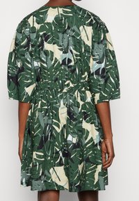 Robe verte à manches courtes avec un imprimé de feuilles tropicales, taille froncée et jupe évasée. Fabriquée en tissu léger avec une texture mate.