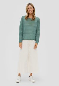Lichtgroene langetermijntrui met een gestructureerd gestreept ontwerp, gecombineerd met crèmekleurige wijde broek en witte sneakers. Eenvoudige en casual outfit.