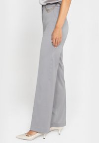 Jasnoszare, dopasowane spodnie o prostym kroju. Posiadają srebrny łańcuszek ozdobny w talii oraz gładkie, teksturowane wykończenie.