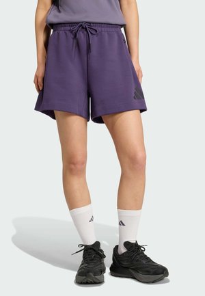 Lilla træningsshorts med elastisk talje, snøre og trykt logo-detalje. Båret med hvide sokker og sorte sneakers.
