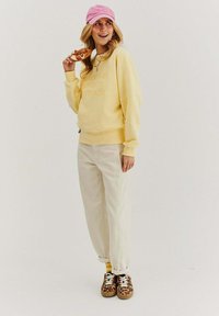 Žltá mikina s embosovaným textom, svetlo béžové nohavice a tenisky s leopardím vzorom. Doplnky tvoria ružová čiapka.