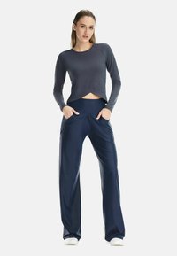 Dunkelgraues Langarmoberteil mit kurzem Saum, kombiniert mit marineblauen, weit geschnittenen Hosen mit Taschen und einer glatten Textur.
