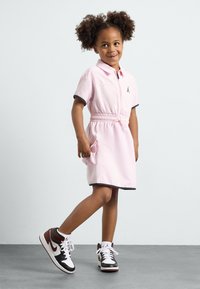 Robe polo rose clair avec des manches courtes, une taille élastique et des finitions noires. Associée à des baskets noires et blanches avec des accents rouges.
