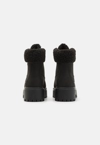 Botas negras hasta el tobillo con suela gruesa, que presentan un suave puño de forro polar texturizado, parte superior de ante y detalles de costura a lo largo de los lados.
