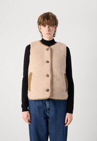 Γούνινο γιλέκο σε μπεζ απόχρωση με μαλακή υφή, που διαθέτει στρογγυλή λαιμόκοψη, πέντε καφέ κουμπιά και δύο πλαϊνές τσέπες σε σκούρο καφέ χρώμα.