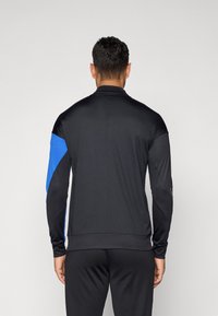 Black athletic jacket with long sleeves; features blue accents on the left arm, smooth texture, and a fitted design for comfort.