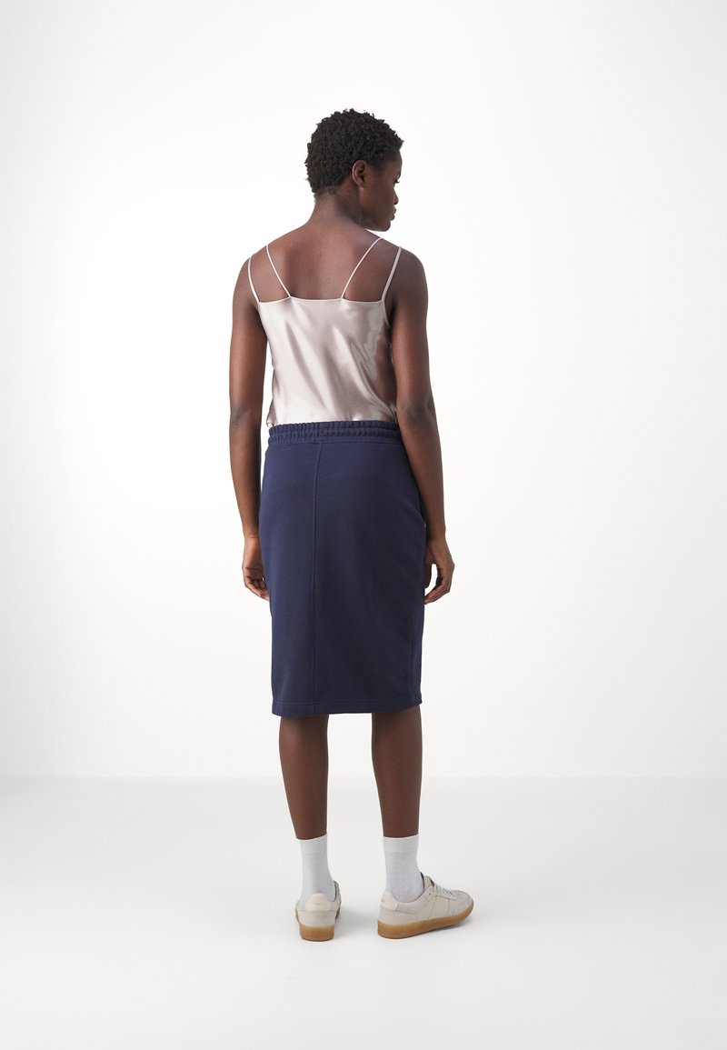 Szatynowa koszulka na ramiączkach w jasnym beżu, w połączeniu z ciemnonawowym, do kolan, spódnicą z elastycznym pasem i gładką teksturą.