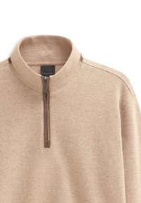 Beiger Fischgrät-Pullover mit einem halben Reißverschluss und Stehkragen. Mit dunkelbraunen Akzenten entlang des Kragens und des Reißverschlusses für Details.