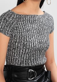 Top de punto acanalado en blanco y negro con escote barco, mangas cortas y tejido texturizado. Combinado con un cinturón de cuero negro con hebilla plateada.