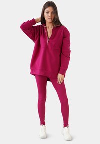 Fuchsia ritssluiting oversized sweatshirt met lange mouwen, gecombineerd met bijpassende strakke leggings. Zachte textuur, minimale stikseldetails.