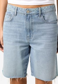 Pantaloni corti di jeans azzurri leggeri con un design classico a cinque tasche, orli sfilacciati e zip, caratterizzati da una chiusura con bottone e un leggero sbiadimento.