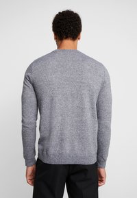 Sweter okrągły dekolt w szarej melanżowej dzianinie, z długimi rękawami i ribbanym wykończeniem. Tekstura wydaje się miękka i przytulna, idealna do noszenia w warstwach.