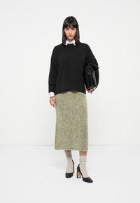 Svart strikkegenser, lysfarget teksturert skjørt, beige knelange sokker og svarte høye hæler. Holder en svart foldover clutch.