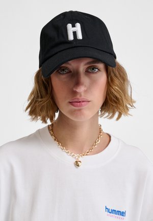 Black baseball cap with white embroidered "H" logo; features a curved brim and adjustable strap. Worn with a white t-shirt and gold chain necklace.