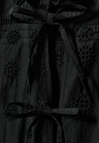 Prenda negra con intrincados círculos bordados, con una cintura atada y tela texturizada, diseñada con detalles de costura visibles.