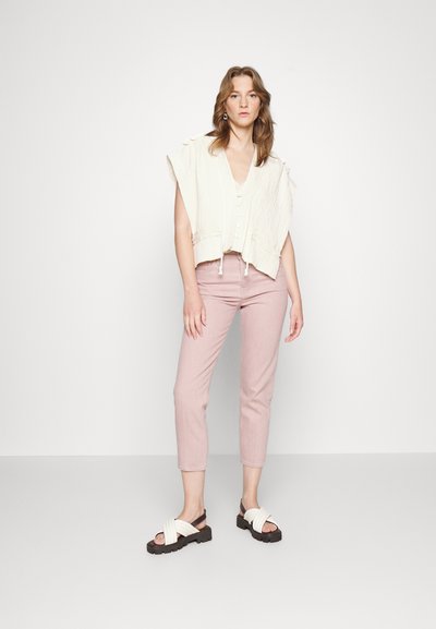 Top cropped leve e off-white com um acabamento texturizado e fecho de botão, combinado com calças rosa de corte slim e sandálias brancas com tiras.