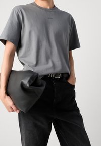 Grijze katoenen T-shirt met korte mouwen en een ronde hals, gecombineerd met zwarte denim broek en een gestructureerde zwarte leren clutch.
