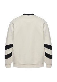 Bluză sportivă crem cu guler negru și două dungi diagonale negre pe fiecare mânecă, vizibilă din spate.