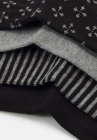 Tres pares de calcetines en negro y gris. Uno tiene un estampado floral, otro es de color gris sólido y el último tiene rayas en negro y gris.