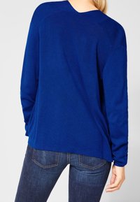 Blå stickad tröja med avslappnad passform, rund halsringning och långa ärmar, kombinerad med mörka denimjeans. Mjuk textur, enkel design.