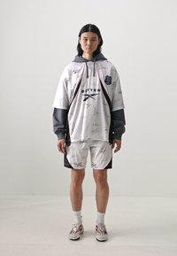 White oversized hoodie with gray accents and signature prints, paired with matching white shorts. Fabric appears lightweight and sporty.