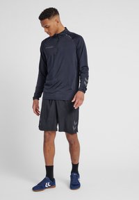 Maglietta atletica a maniche lunghe blu con zip a quarto, pantaloni corti neri e scarpe sportive blu. Dotata di accenti riflettenti e textures liscia.