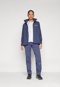 Jachetă impermeabilă de marină cu glugă și logo Terrex, asociată cu pantaloni asortați. Material fin și ușor; design practic pentru îmbrăcăminte activă.
