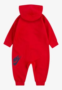 Crveni kombinezon s kapuljačom napravljen od pamuka, s dugim rukavima i elastičnim manžetama, s tamnoplavi Nike logo na lijevoj nozi.