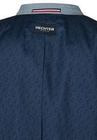 Marineblaue Jacke mit strukturiertem Muster, einem hellblauen Kragen und einem schwarzen Etikett mit "HECHTER PARIS." Rote und weiße Akzentstreifen am Kragen.